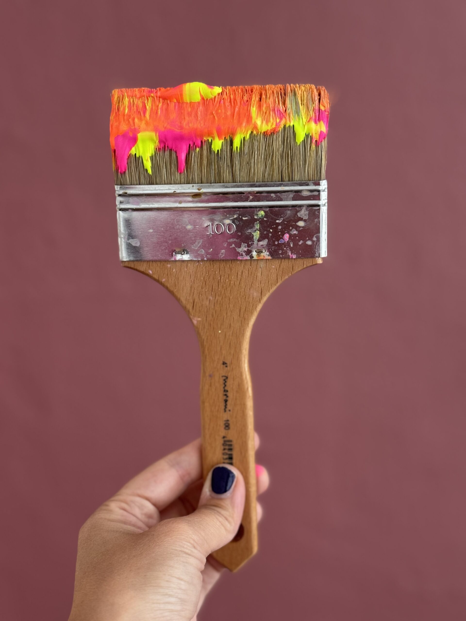 Großer Pinsel mit bunten Farben vor farbiger Wand – Werkzeug für freies Malen.