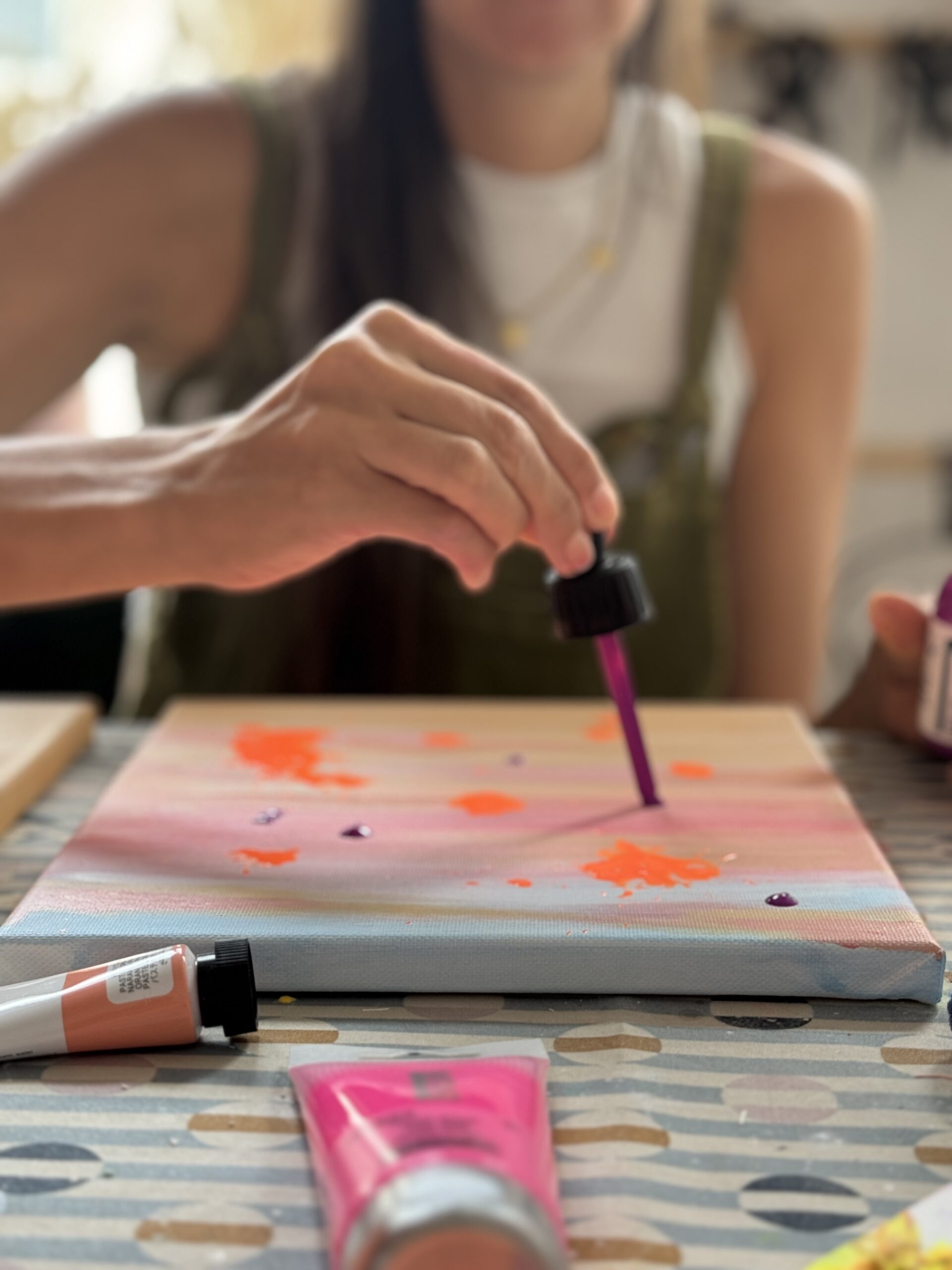 Teilnehmerin arbeitet mit Pipette an einem Bild mit Himmel und Farbspritzern – Fokus auf Detailarbeit.